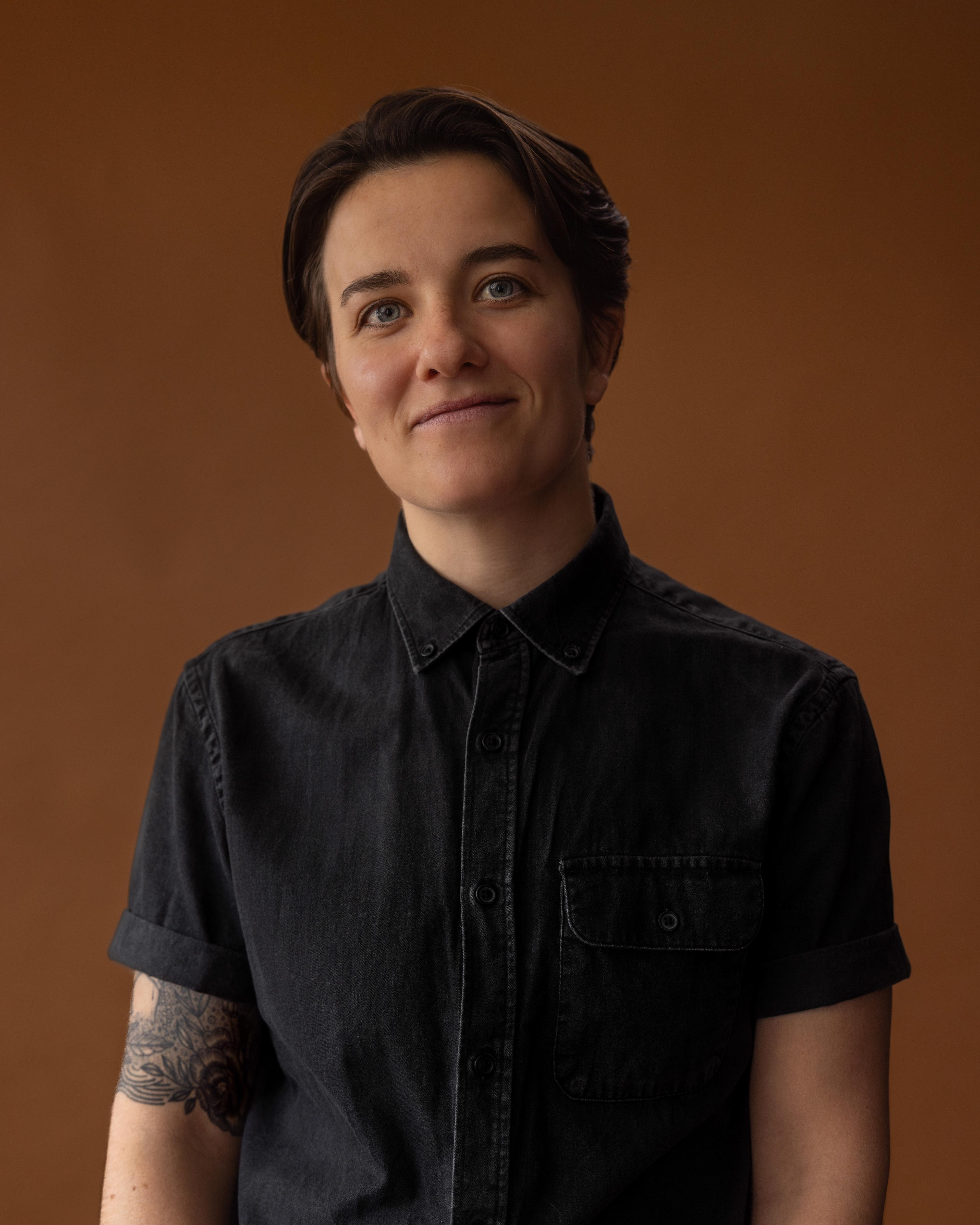 A non-binary person looks directly at the camera, smiling.