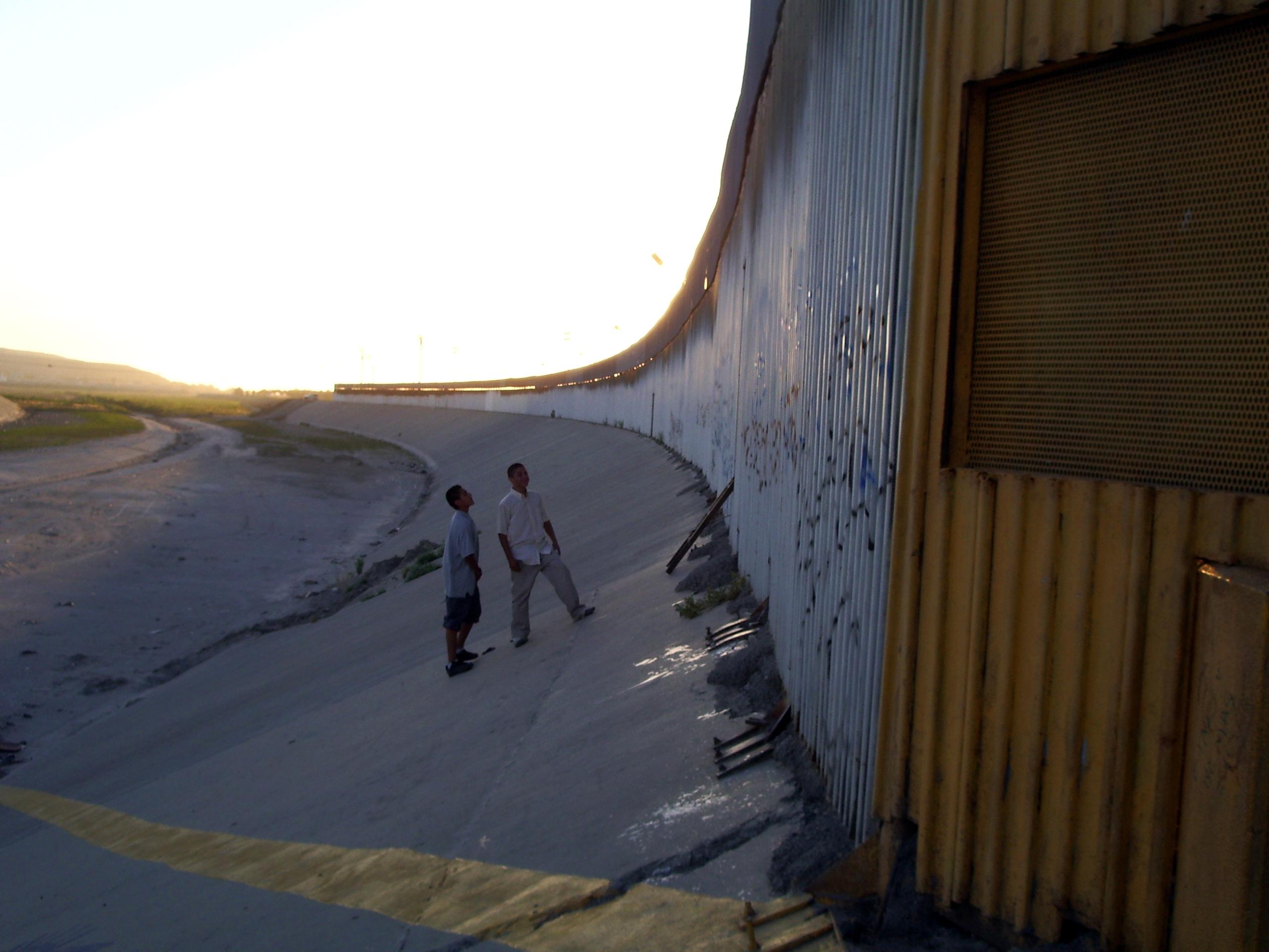 Two young boys stand at the border of Mexico and the United States.