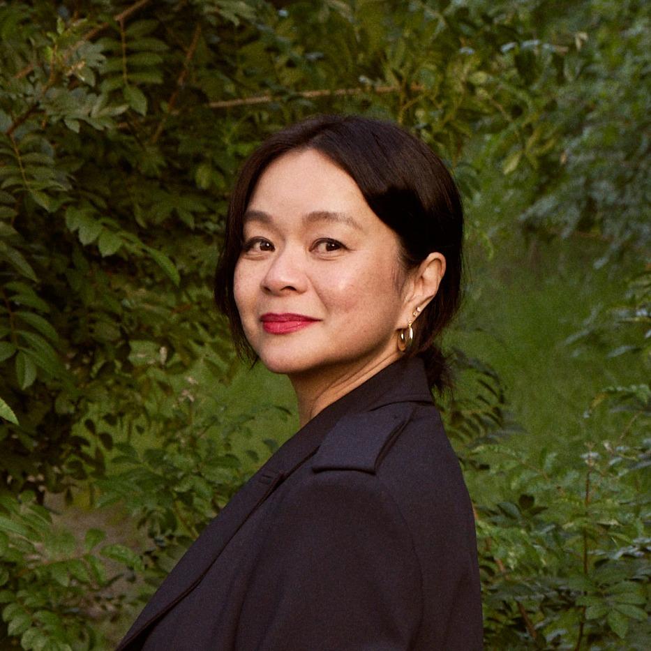 Asian woman, black hair, wearing navy blue blazer, hair pulled back.