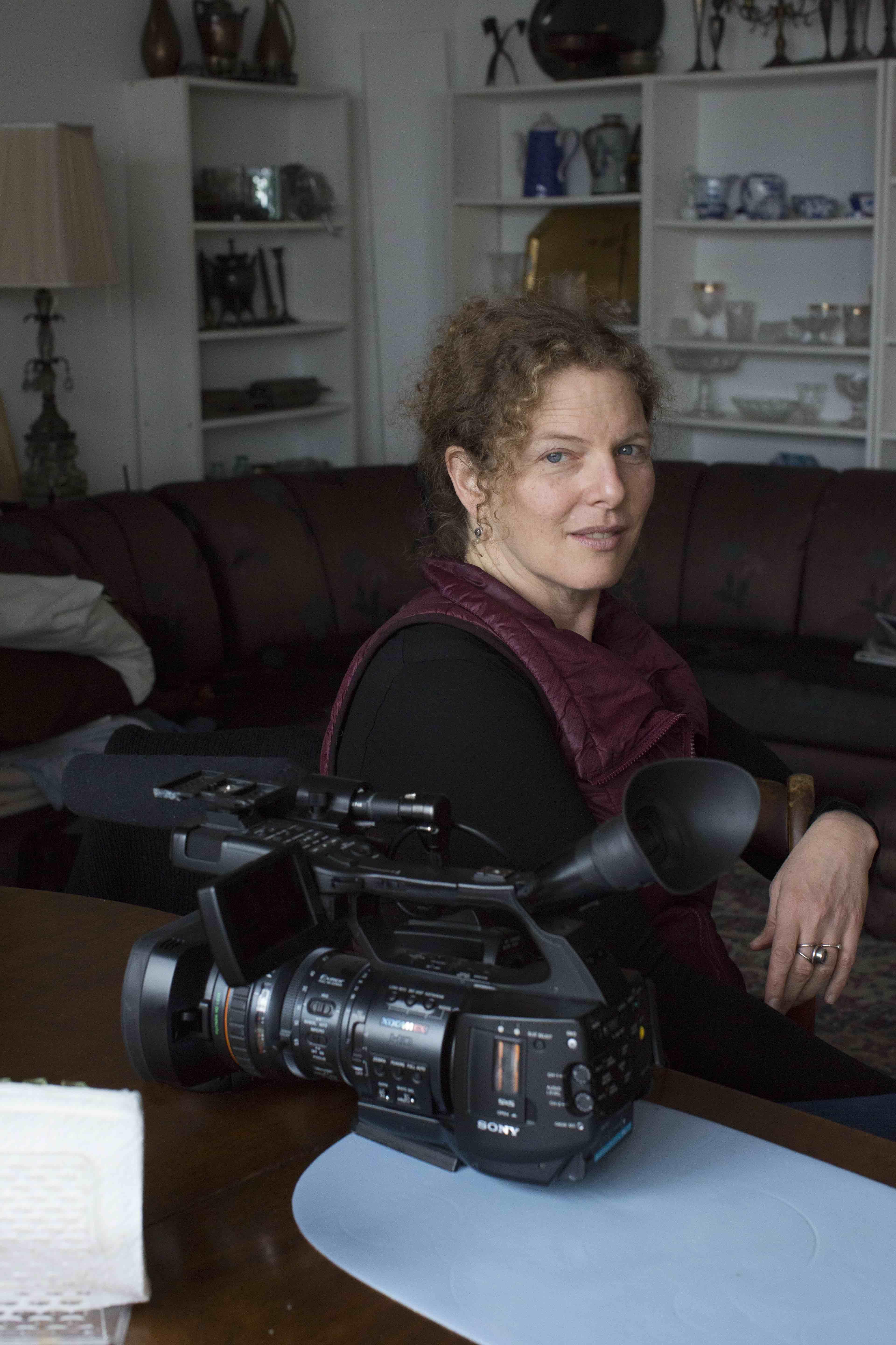 Deirdre Fishel is smiling with a camera in front of her.