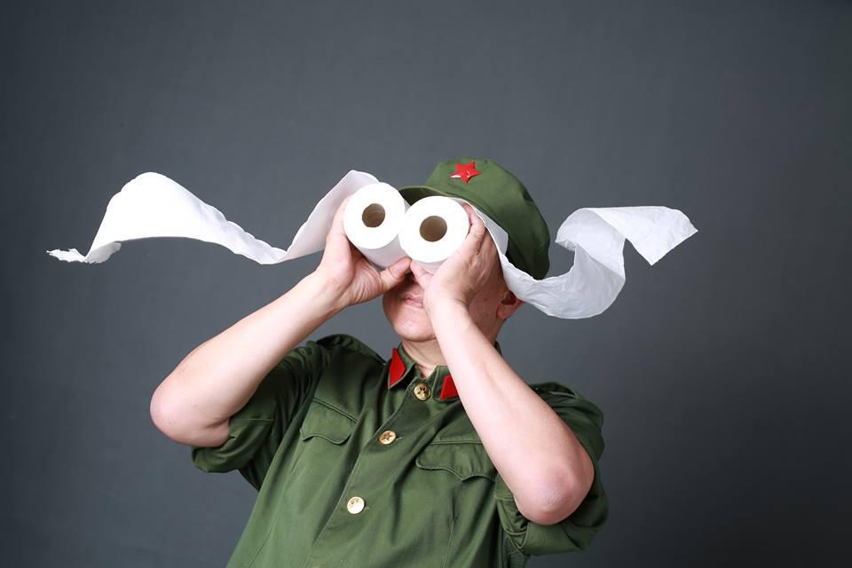 A man wearing an army uniform holds two rolls of toilet paper up to his eyes.