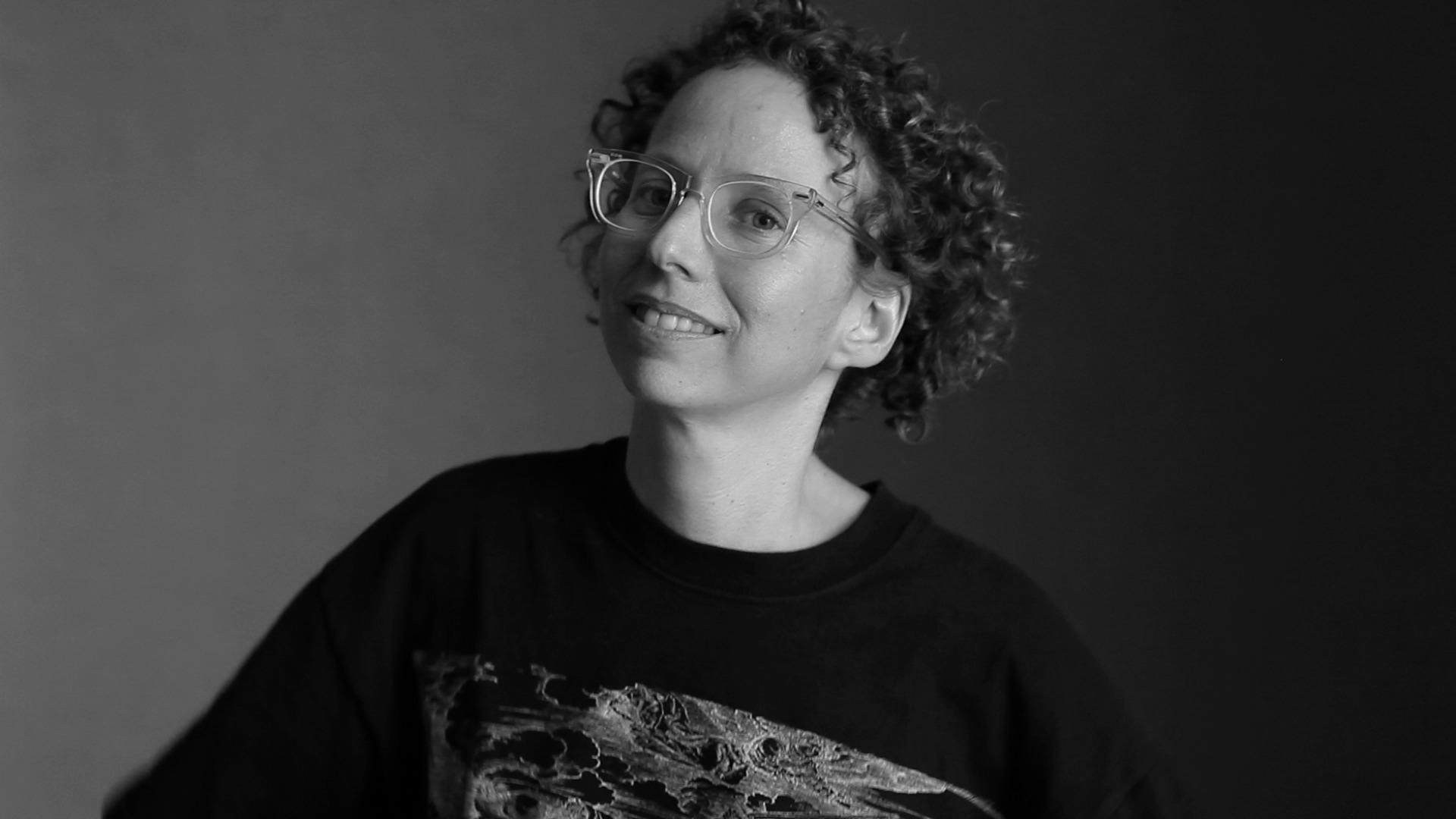 Jennie Livingston looks at the camera and smiles. She wears eyeglasses. Portrait in black and white.