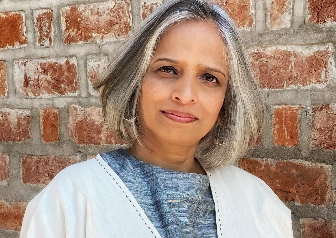 Nistha Jain stands in front of a brick wall. She has shoulder-length hair and wears a blue and white blouse.