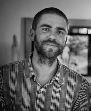 A black and white portrait of a man wearing a button down smiling and looking into the camera.