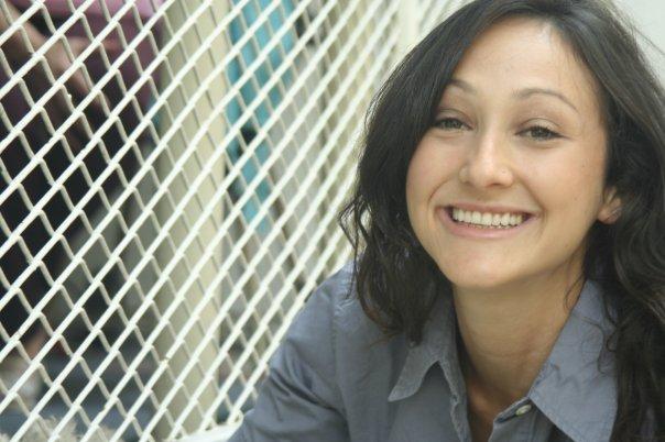 A portrait of a woman in front of a fence smiling at the camera.
