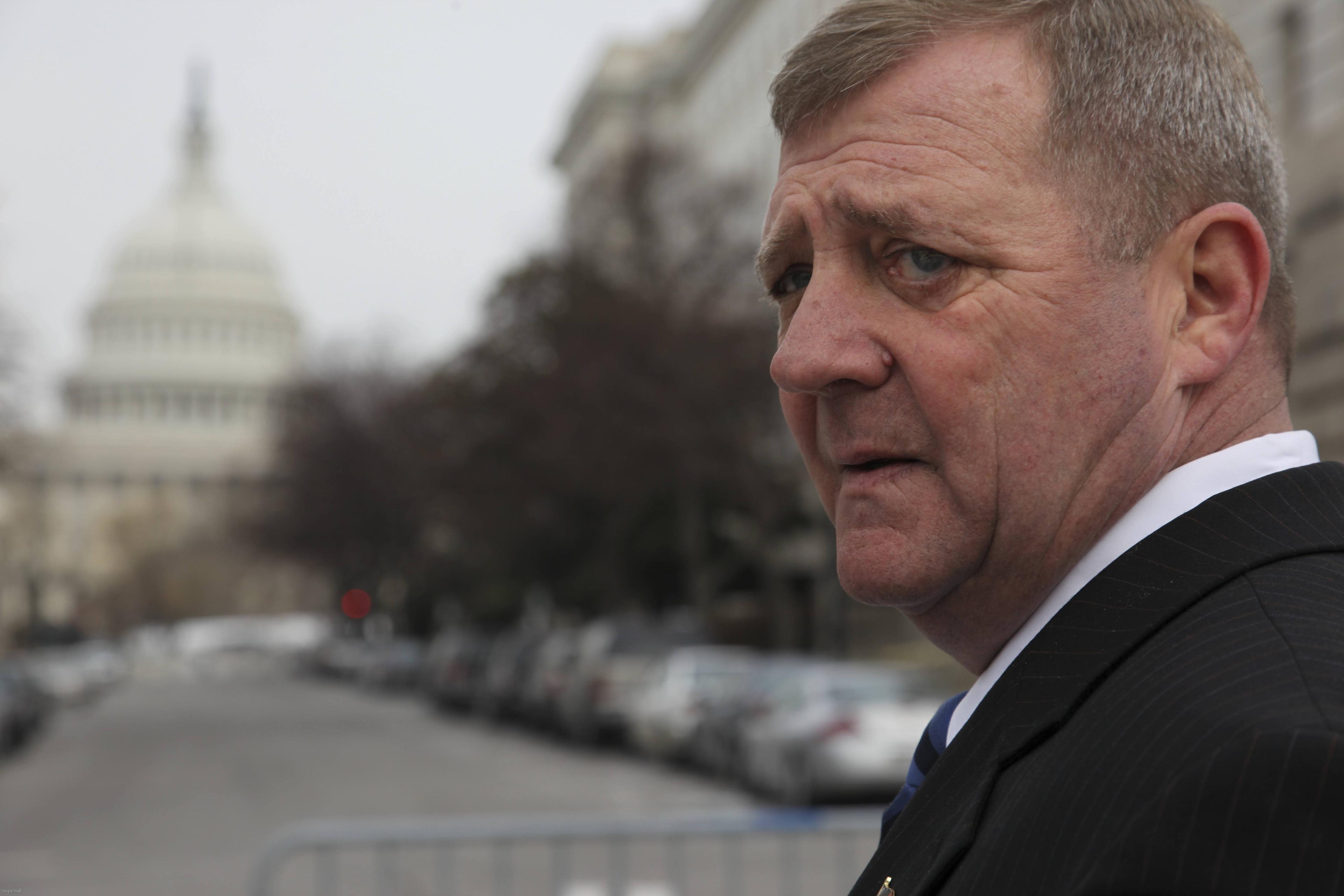 A man looks over his shoulder with a concerned expression. He is down the street from the Capitol building.