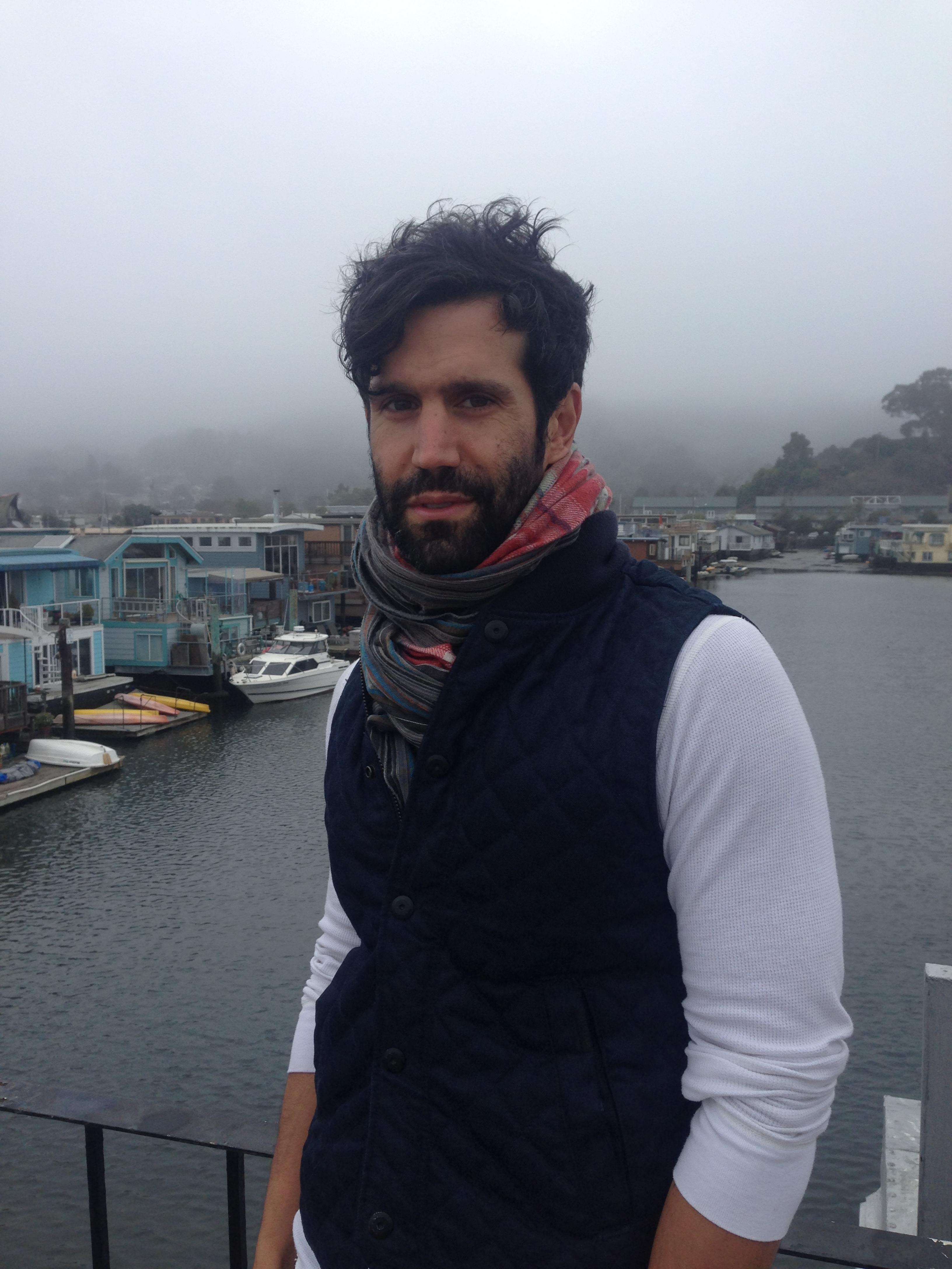 Christopher LaMarca looks at the camera with a slight smile. He is standing in front of a body of water.