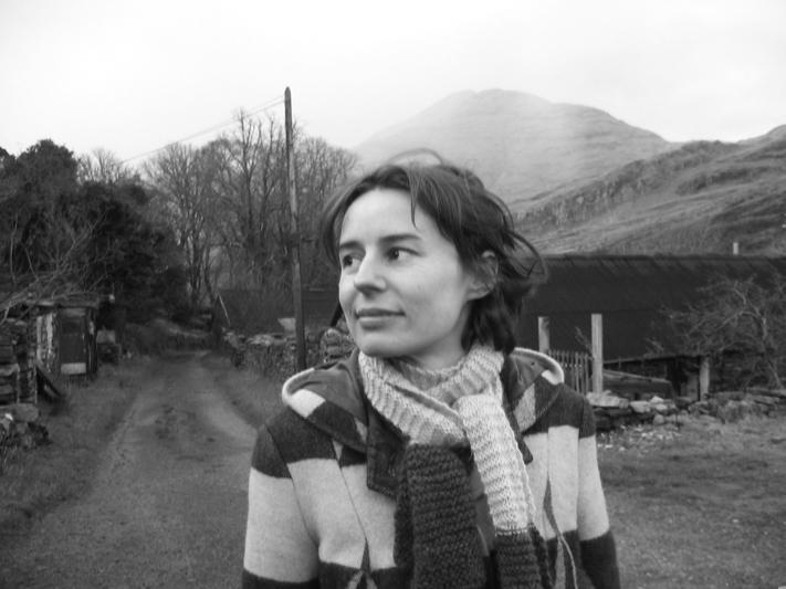 A black and white portrait of a woman in front of a mountain landscape looking off camera.