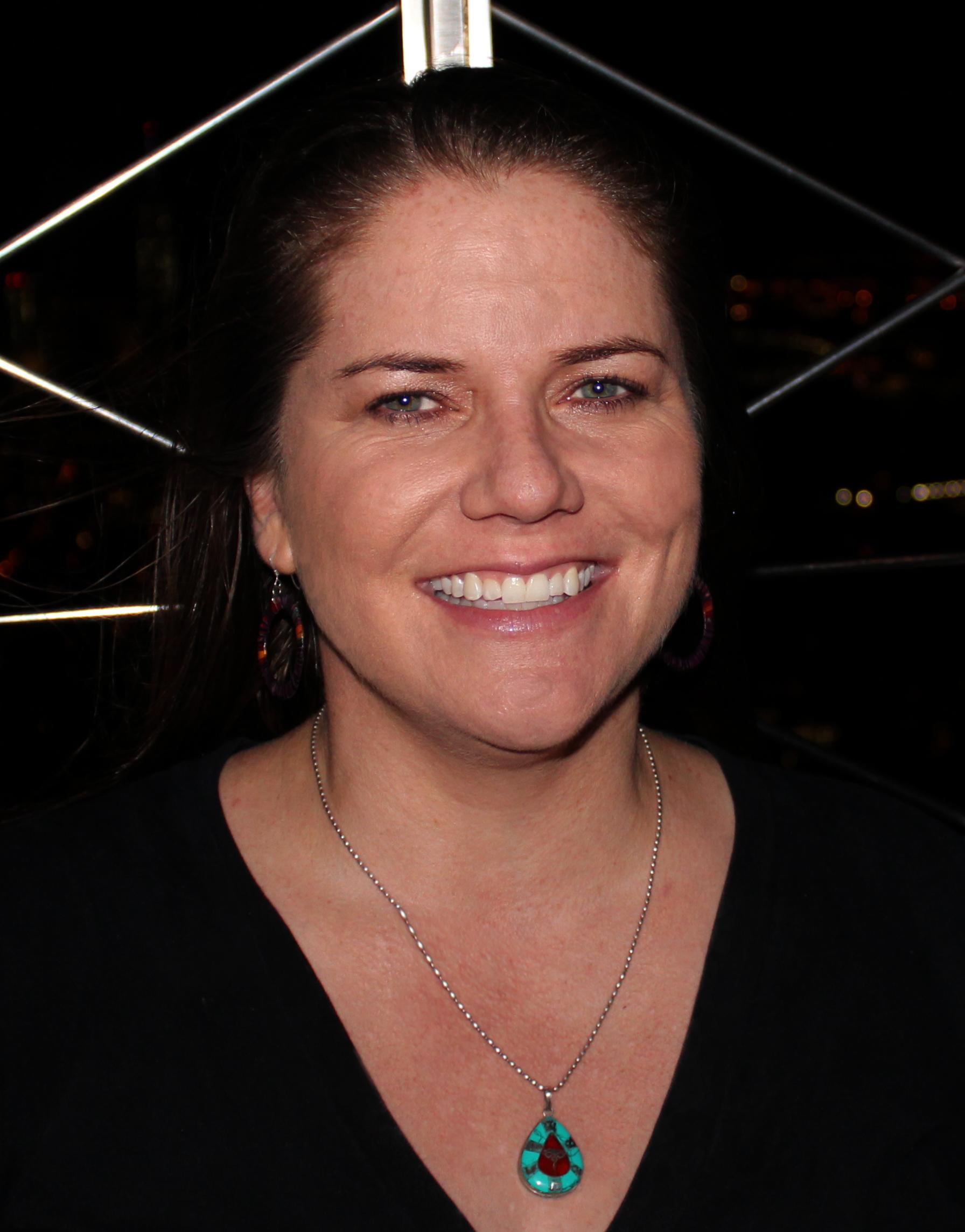 A portrait of a woman wearing a turquoise pendant necklace smiling at the camera.