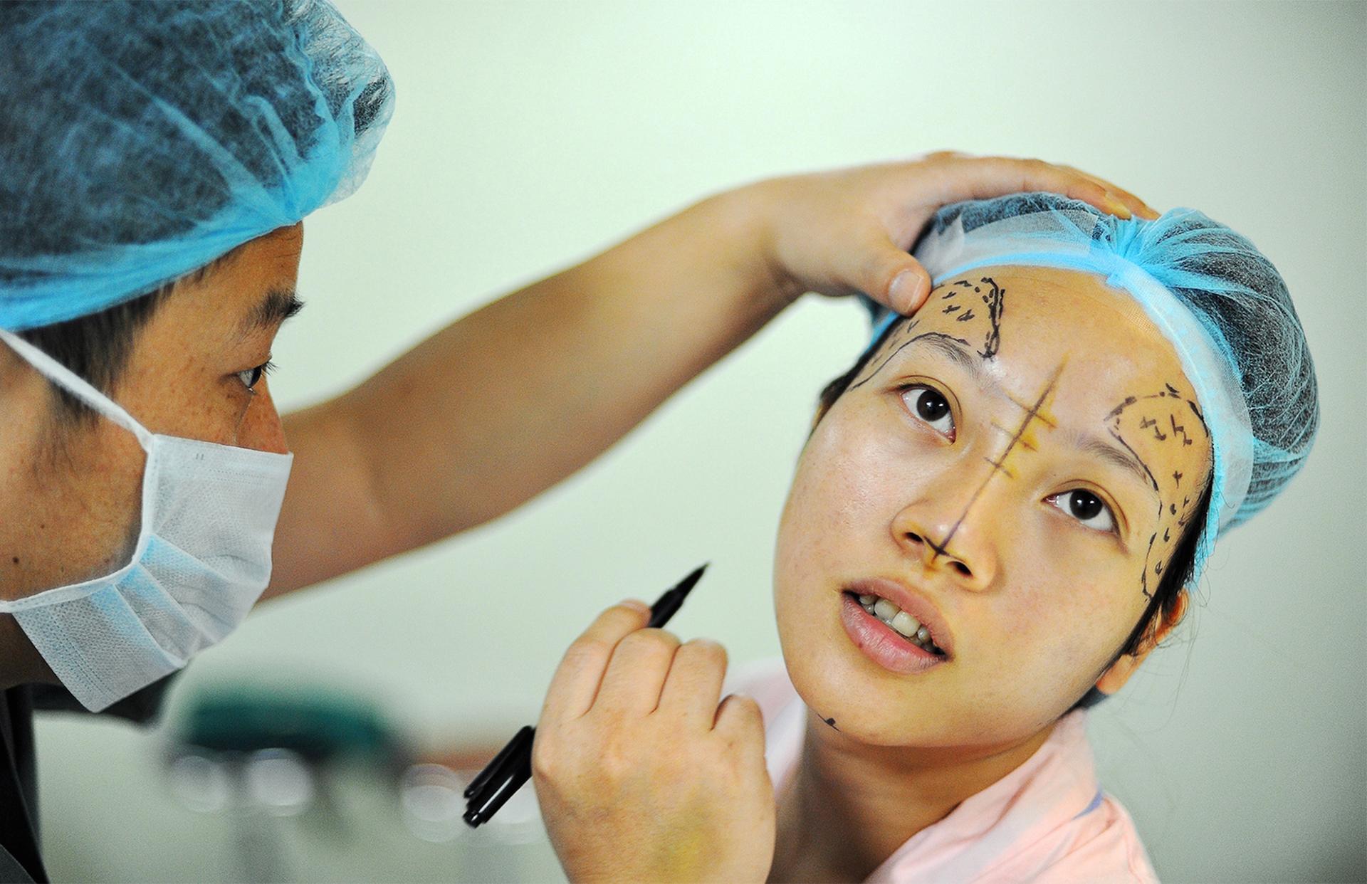 A woman gets a cosmetic surgery consultation. A surgeon makes markings and diagrams on her face.