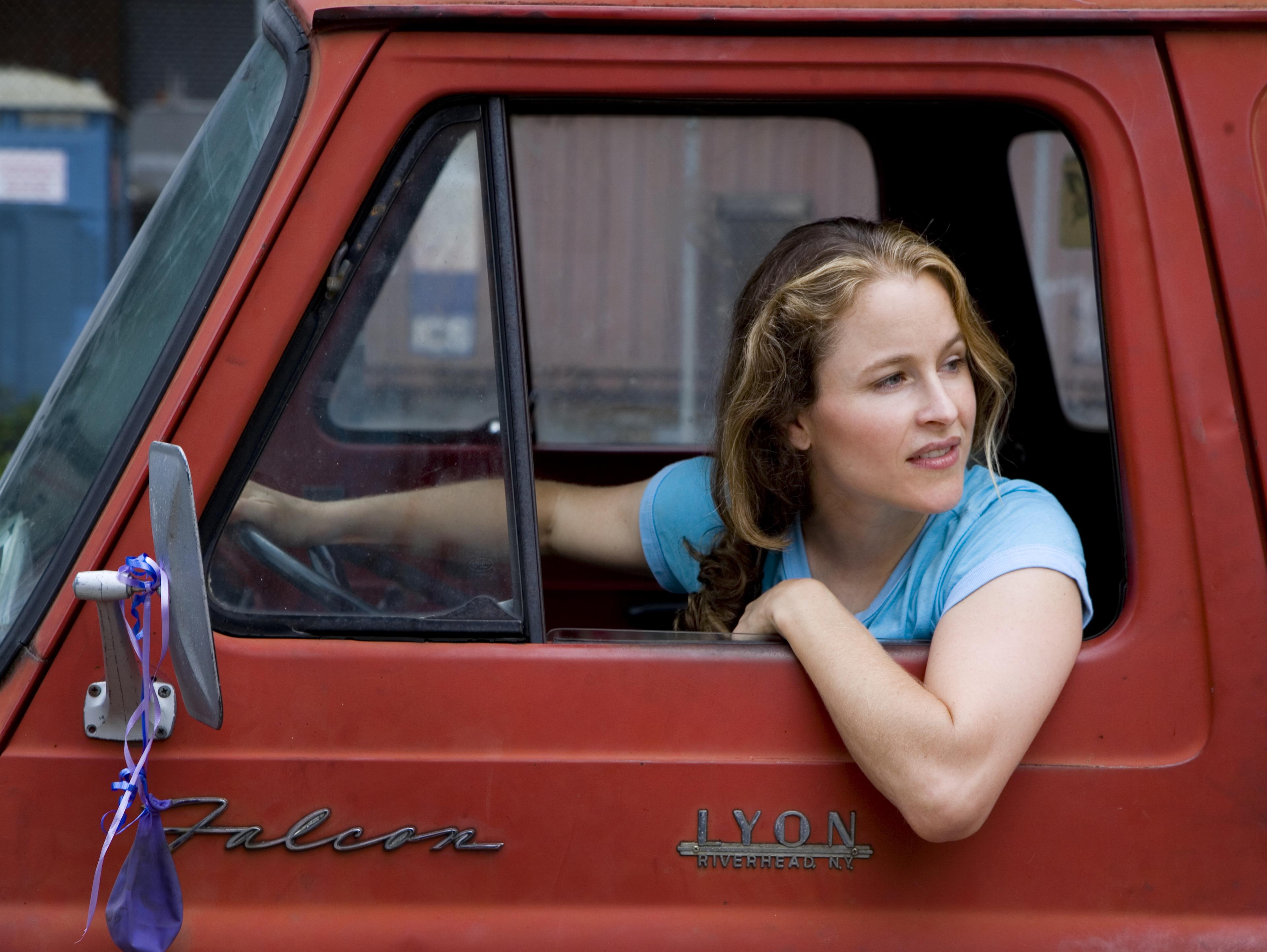 A woman driving a retro car hooks her elbow on the window and looks behind the car.