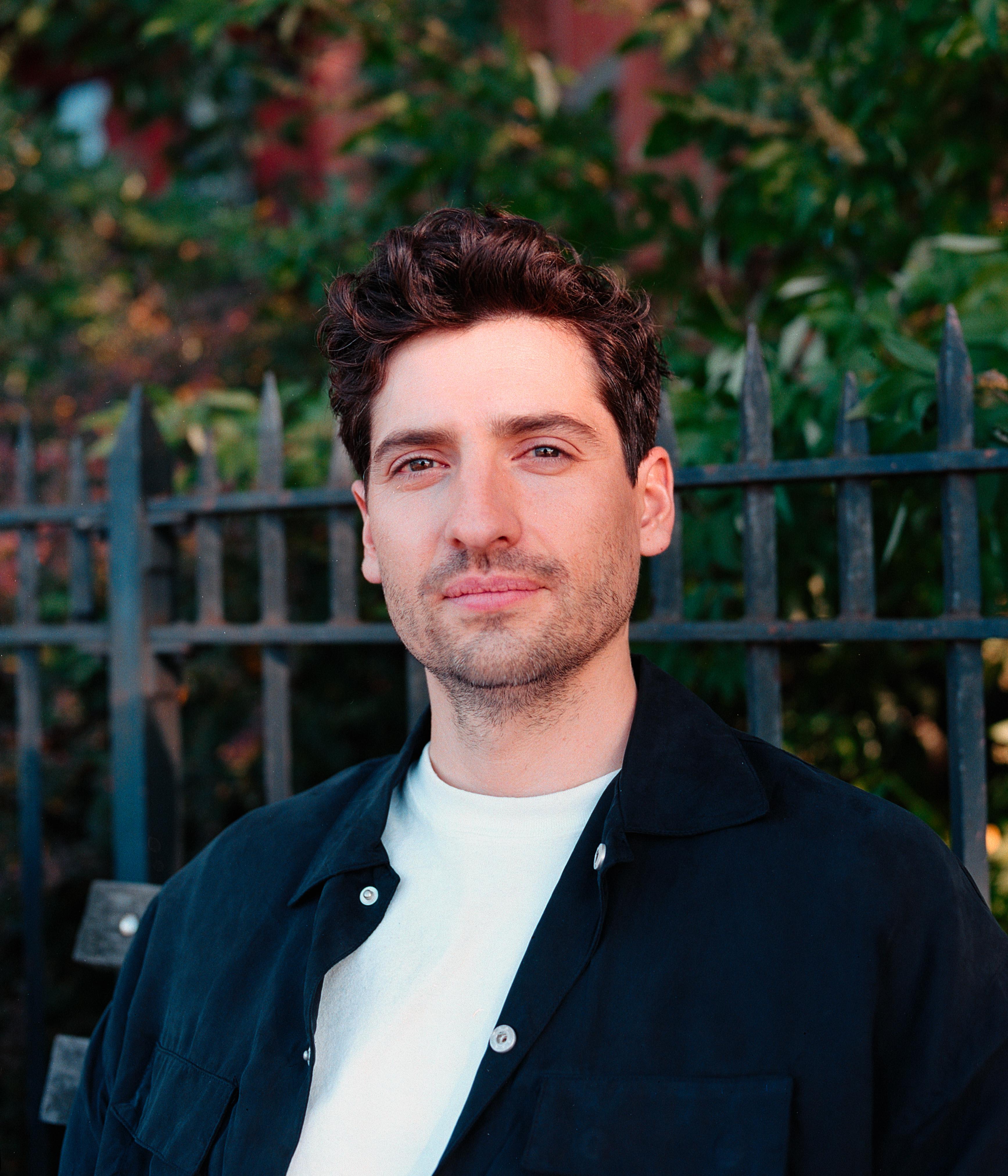 A portrait of a man sitting on a bench in front of a brownstone home.