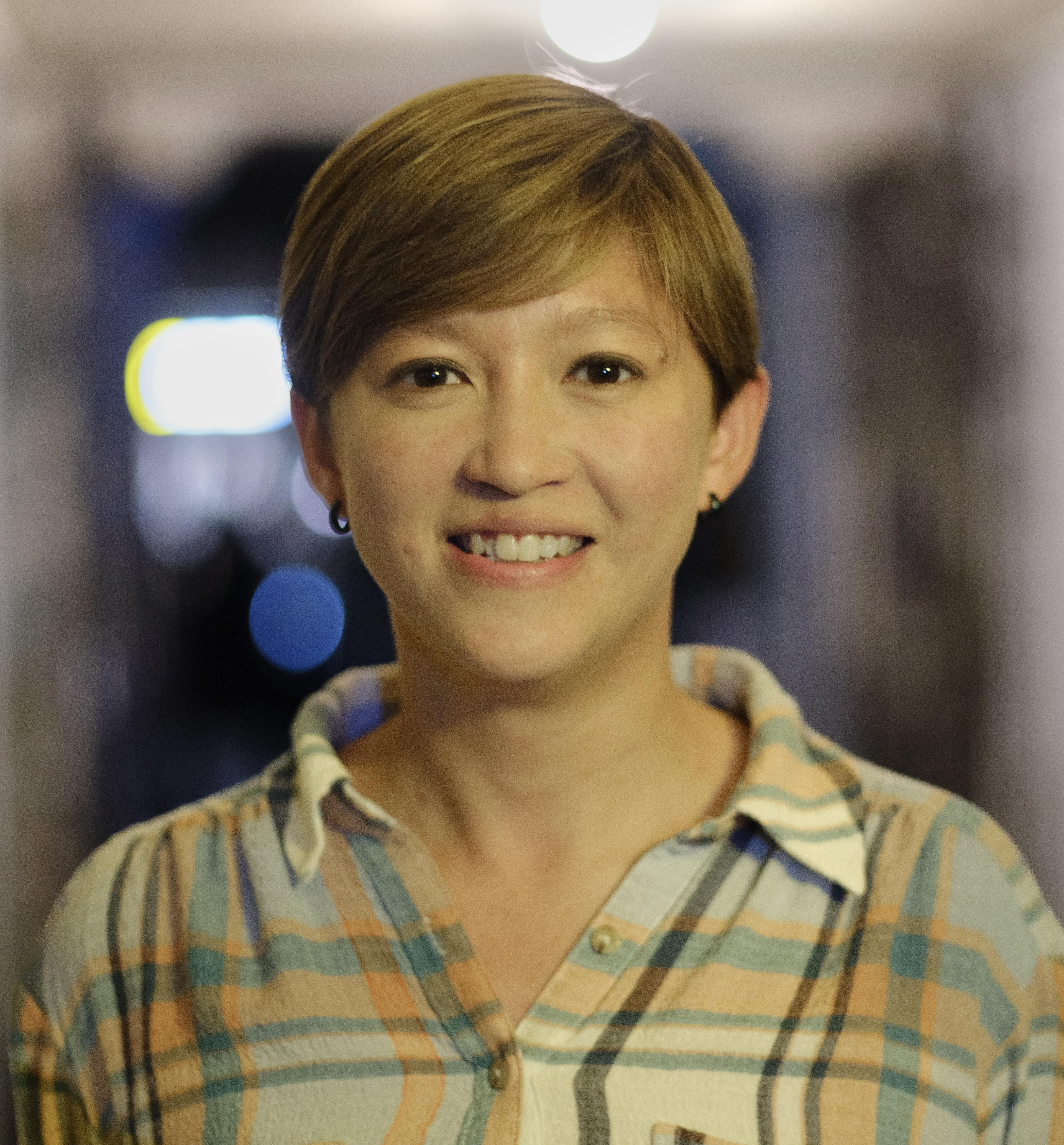 A portrait of a woman wearing a plaid shirt smiling into the camera.