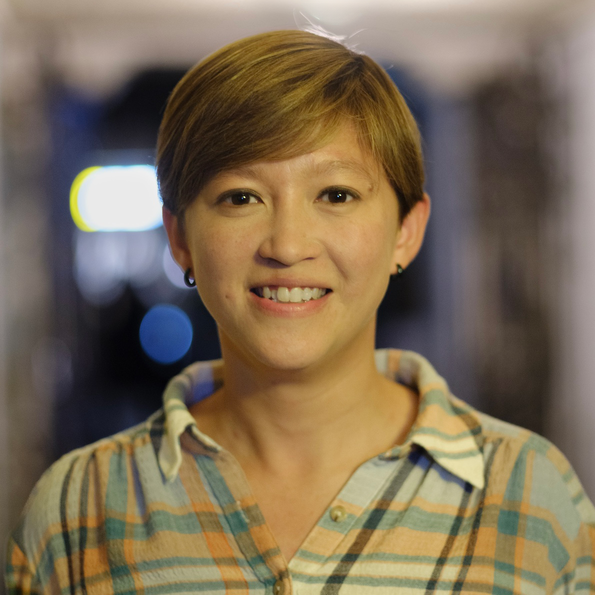 A portrait of a woman wearing a plaid shirt smiling into the camera.