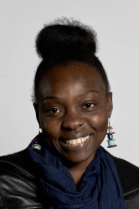 A portrait of a woman with her hair in a bun and colorful chunky earrings smiling at the camera.