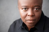 A photo of a man in front of a grey backdrop looking into the camera.