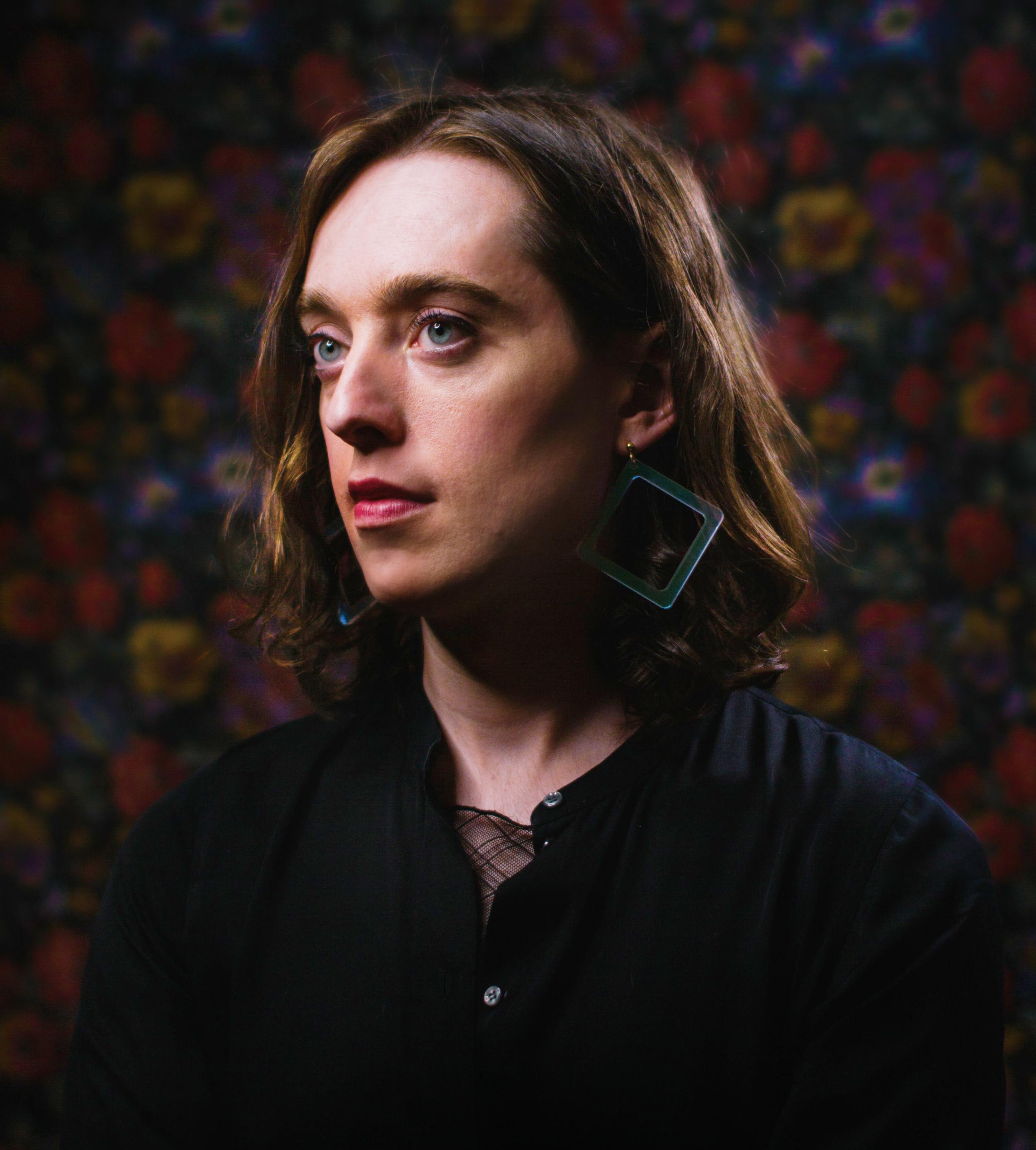 A portrait of a person in front of a floral background, looking off camera.