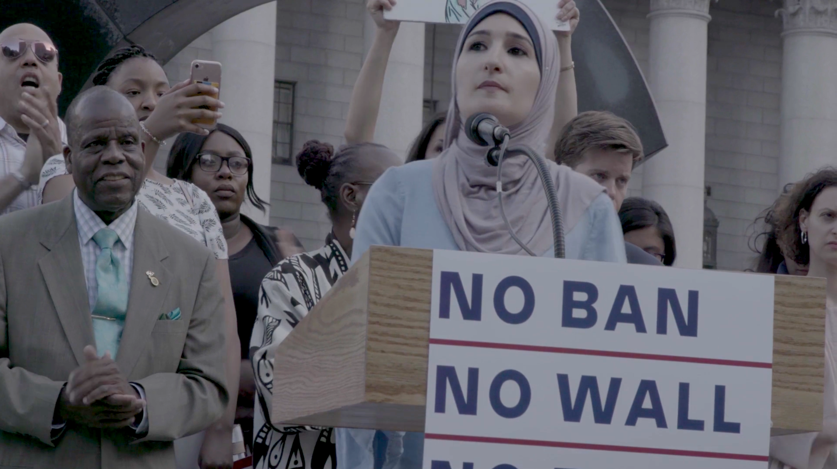 A person is standing on a podium that reads, "No Ban. No Wall."