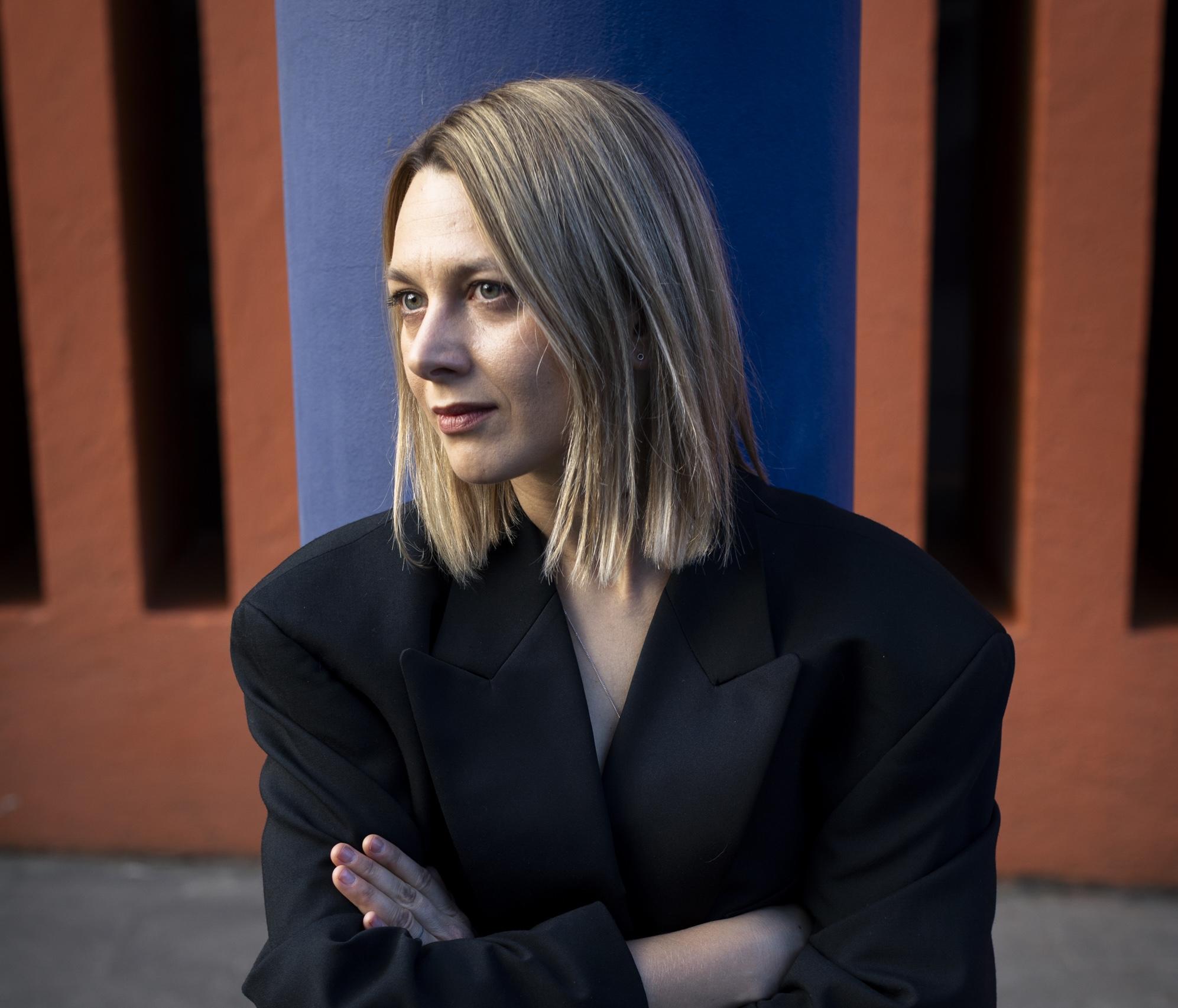Oksana Karpovych looking to the side and wearing a black pantsuit.