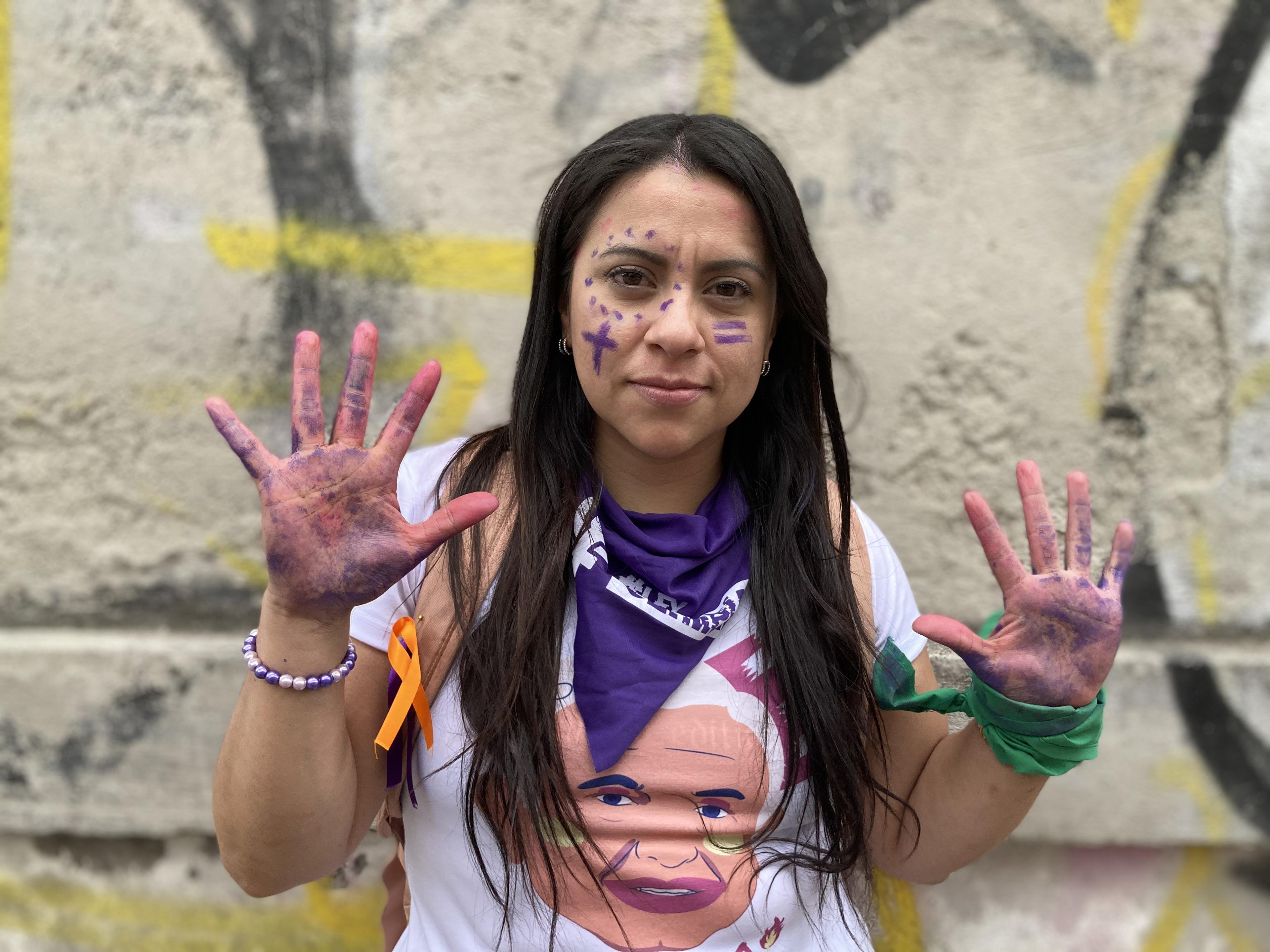 A person holds up their hands with purple paint on it.