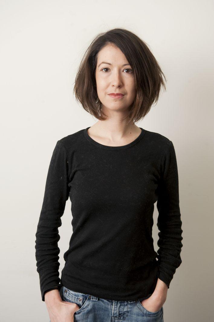 A medium shot of a woman with her hands tucked into her jeans pockets looking into the camera.