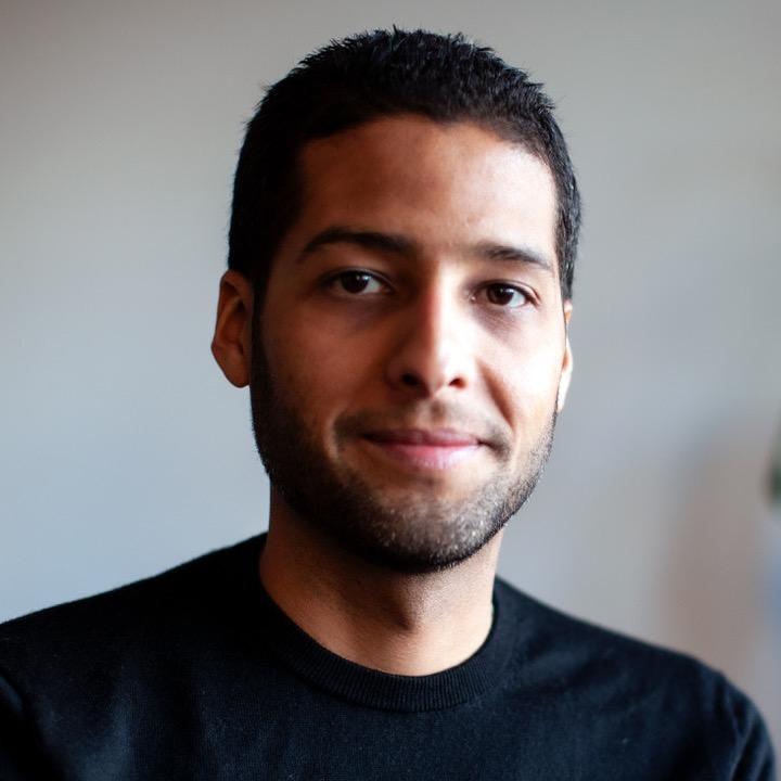 A man stands in front of a house plant and smiles at the camera.