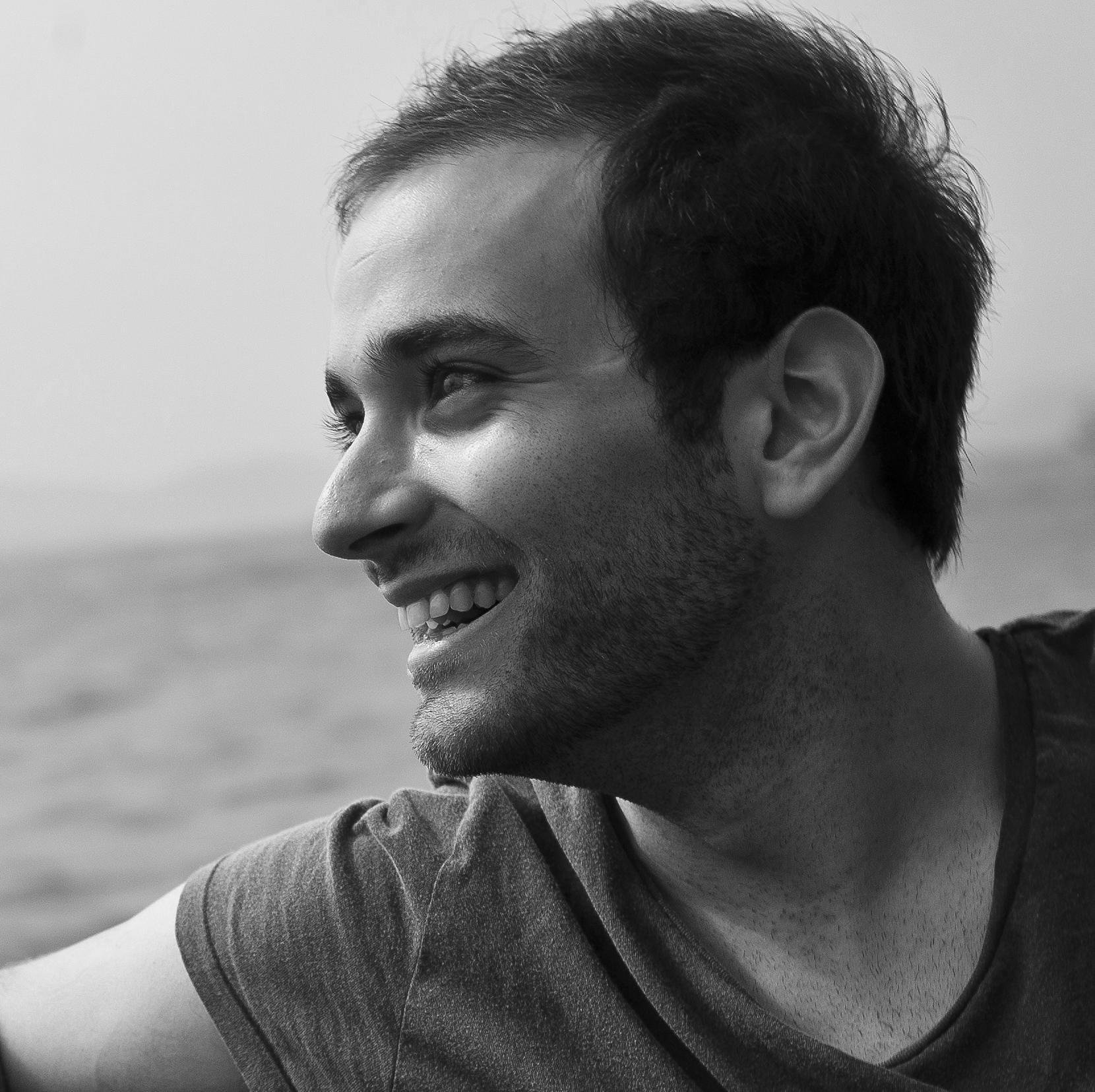 A black and white photo of a man on a boat looking out over the water and smiling.