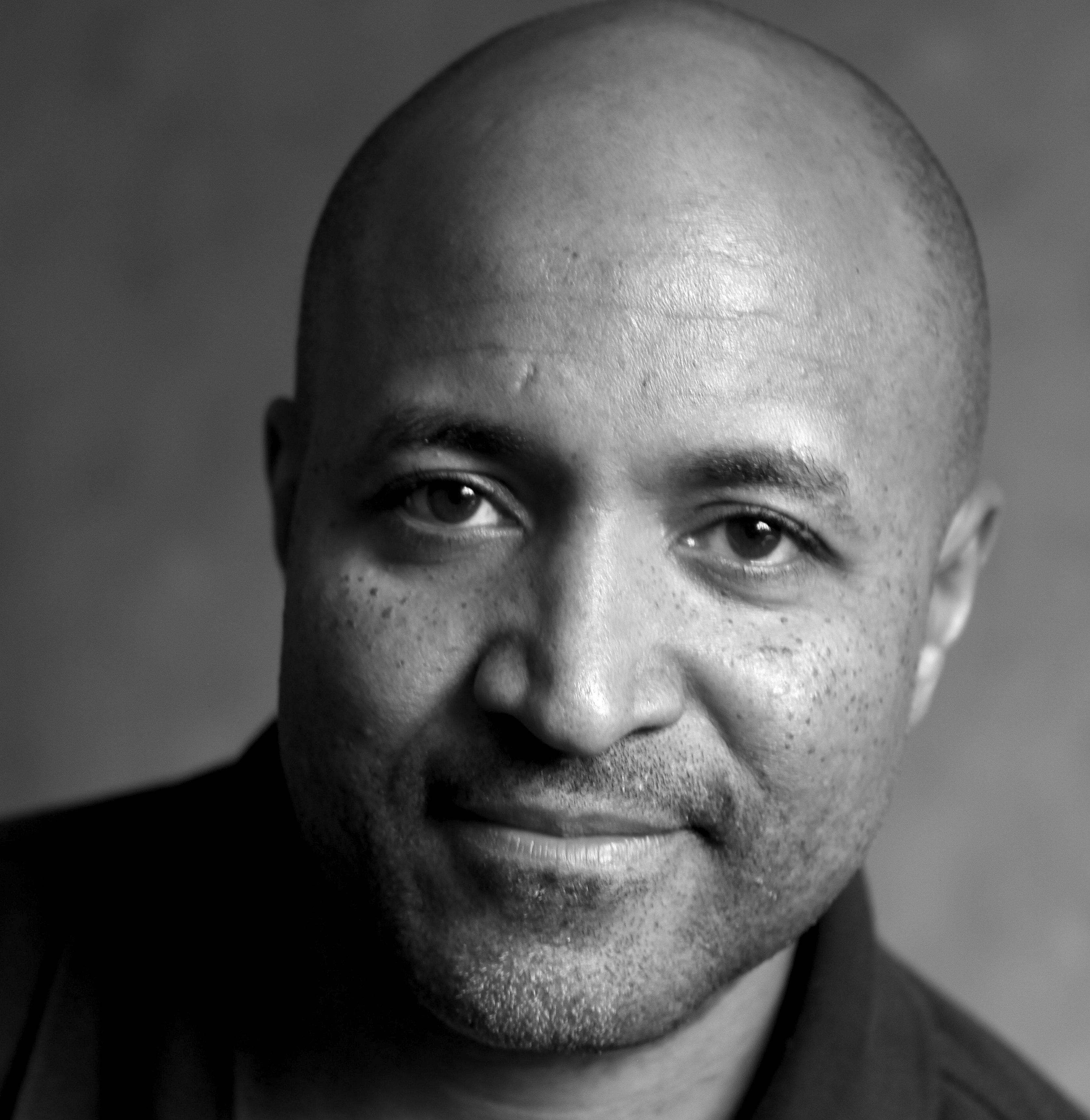 A black and white headshot of a man smiling into the camera.