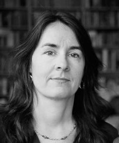 A black and white portrait of a woman in front of a bookshelf.