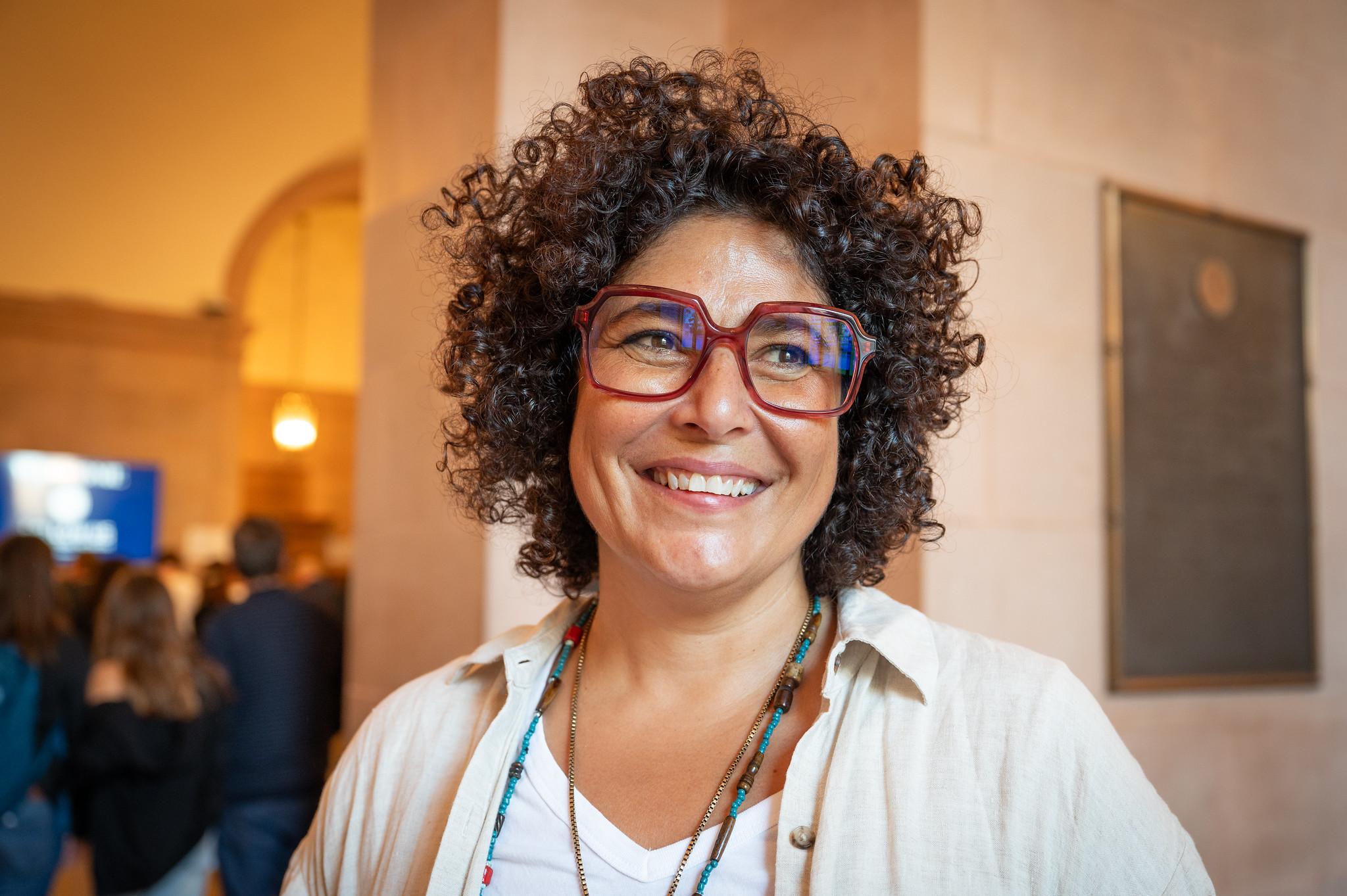 woman with brown curly hair and large glasses smiling