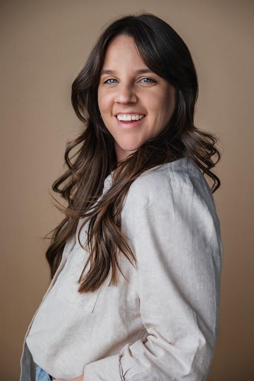 A woman with dark, long hair smiles, looking at the camera.