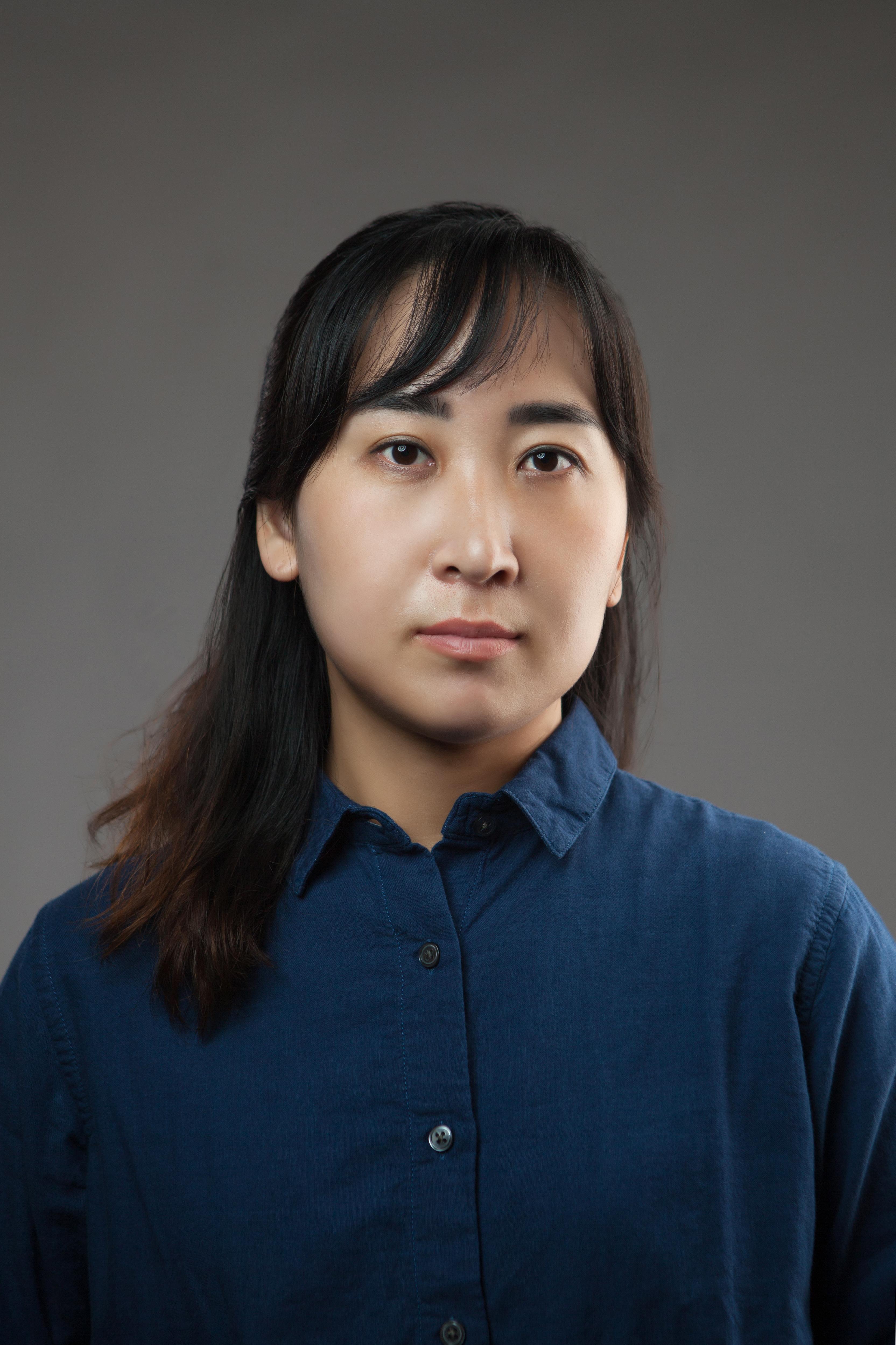 Juyeon Yang is looking straight into the camera, wearing a blue button-up shirt.
